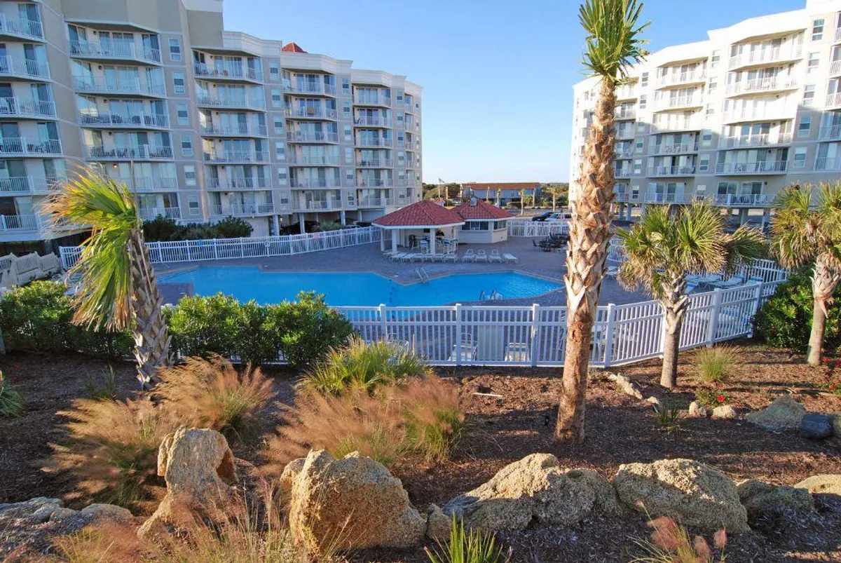 A lively outdoor swimming pool surrounded by palm trees, resort buildings, and a poolside gazebo. The area is designed for swimming, sunbathing, and socializing, evoking a cheerful and inviting atmosphere.