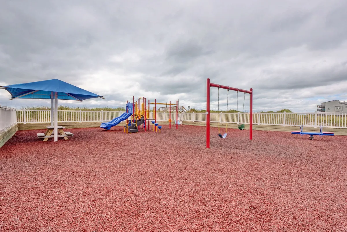 A colorful playground featuring swings, playground equipment, a picnic area, and a fenced yard where children play and families gather. The mood is joyful and welcoming, highlighting activities for younger guests.