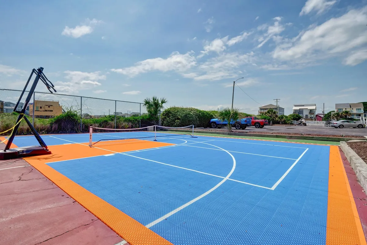 This exterior image showcases a vibrant sports court with a basketball hoop, tennis net, and colorful surface. The scene is outdoors, evoking a lively, energetic atmosphere ideal for recreation and wellness activities.