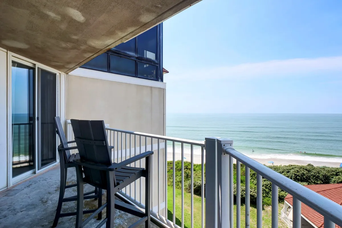 An inviting balcony with cozy seating overlooking the ocean and sandy beachfront. The scene captures the tranquility of oceanfront living, perfect for enjoying a sunrise or a romantic evening under the stars.