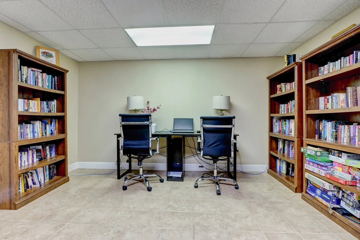 This image shows a well-lit business center featuring bookshelves, desks, chairs, and a computer, designed for productivity and quiet work.