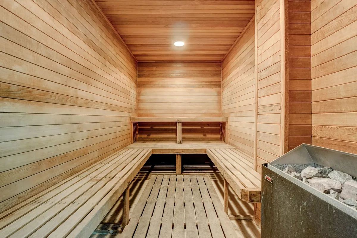 A serene sauna room featuring wooden benches, a sauna stove, and wood-paneled walls. The tranquil atmosphere invites moments of relaxation and wellness after a workout or swim.